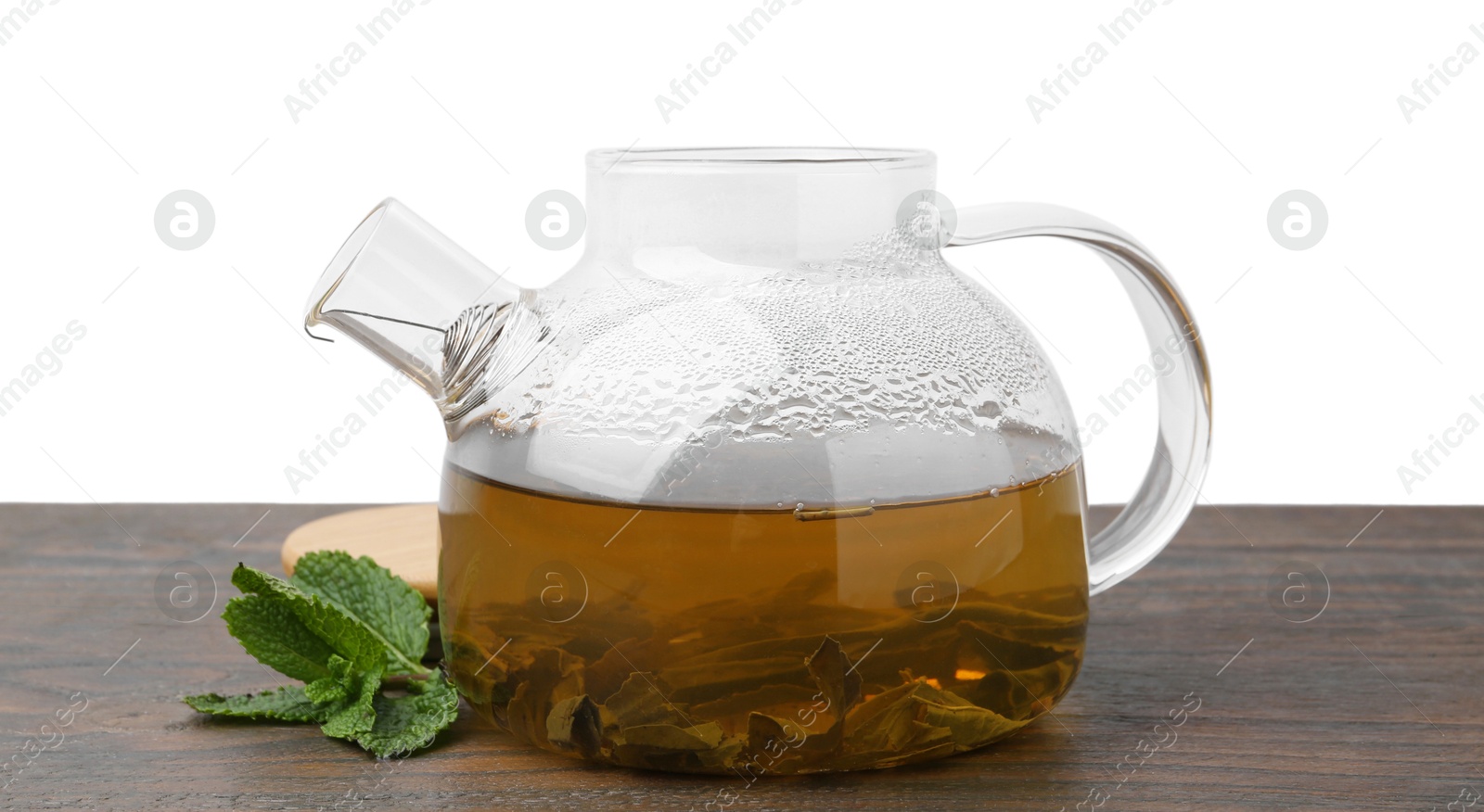 Photo of Aromatic mint tea in glass teapot and fresh leaves on wooden table against white background