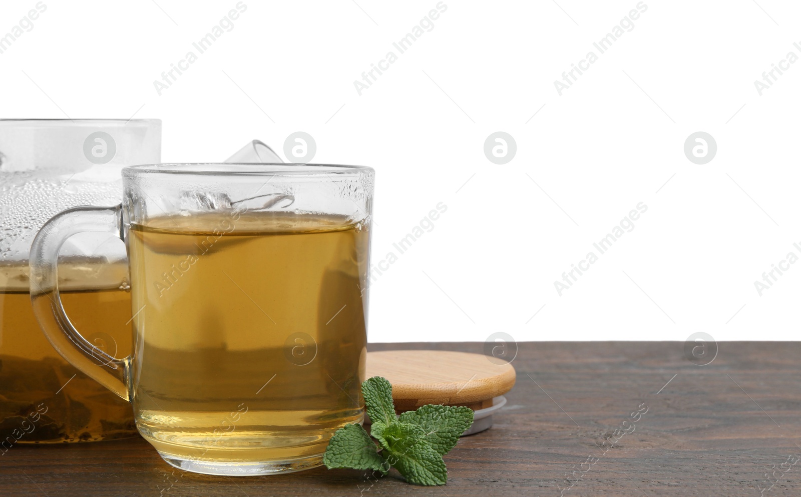 Photo of Aromatic mint tea in glass cup and fresh leaves on wooden table against white background, space for text