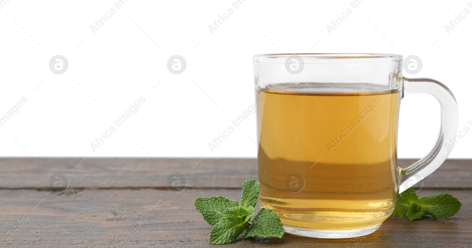 Photo of Aromatic mint tea in glass cup and fresh leaves on wooden table against white background, space for text