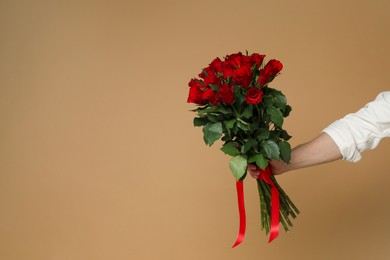 Photo of Happy Valentine's Day. Man with bouquet of roses on brown background, closeup. Space for text