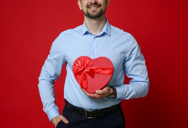 Photo of Happy Valentine's Day. Man with heart shaped gift box on red background, closeup