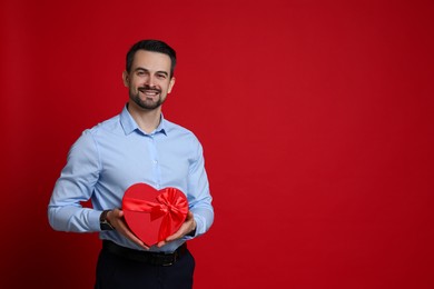 Photo of Happy Valentine's Day. Handsome man with heart shaped gift box on red background. Space for text