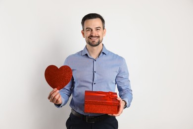 Photo of Happy Valentine's Day. Handsome man with paper heart and gift on white background