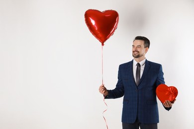 Photo of Happy Valentine's Day. Handsome man with heart shaped balloon and gift box on white background. Space for text