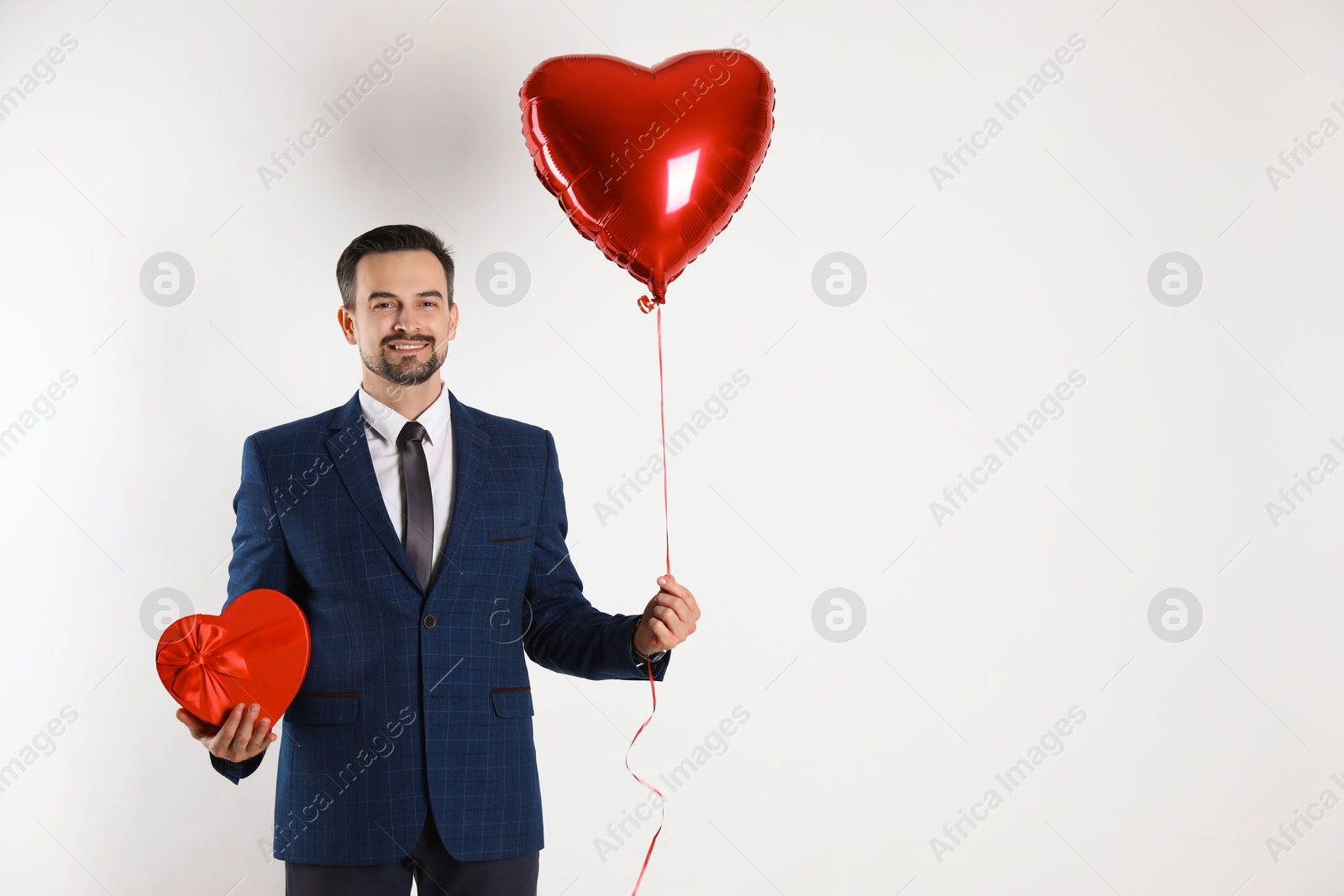 Photo of Happy Valentine's Day. Handsome man with heart shaped balloon and gift box on white background. Space for text