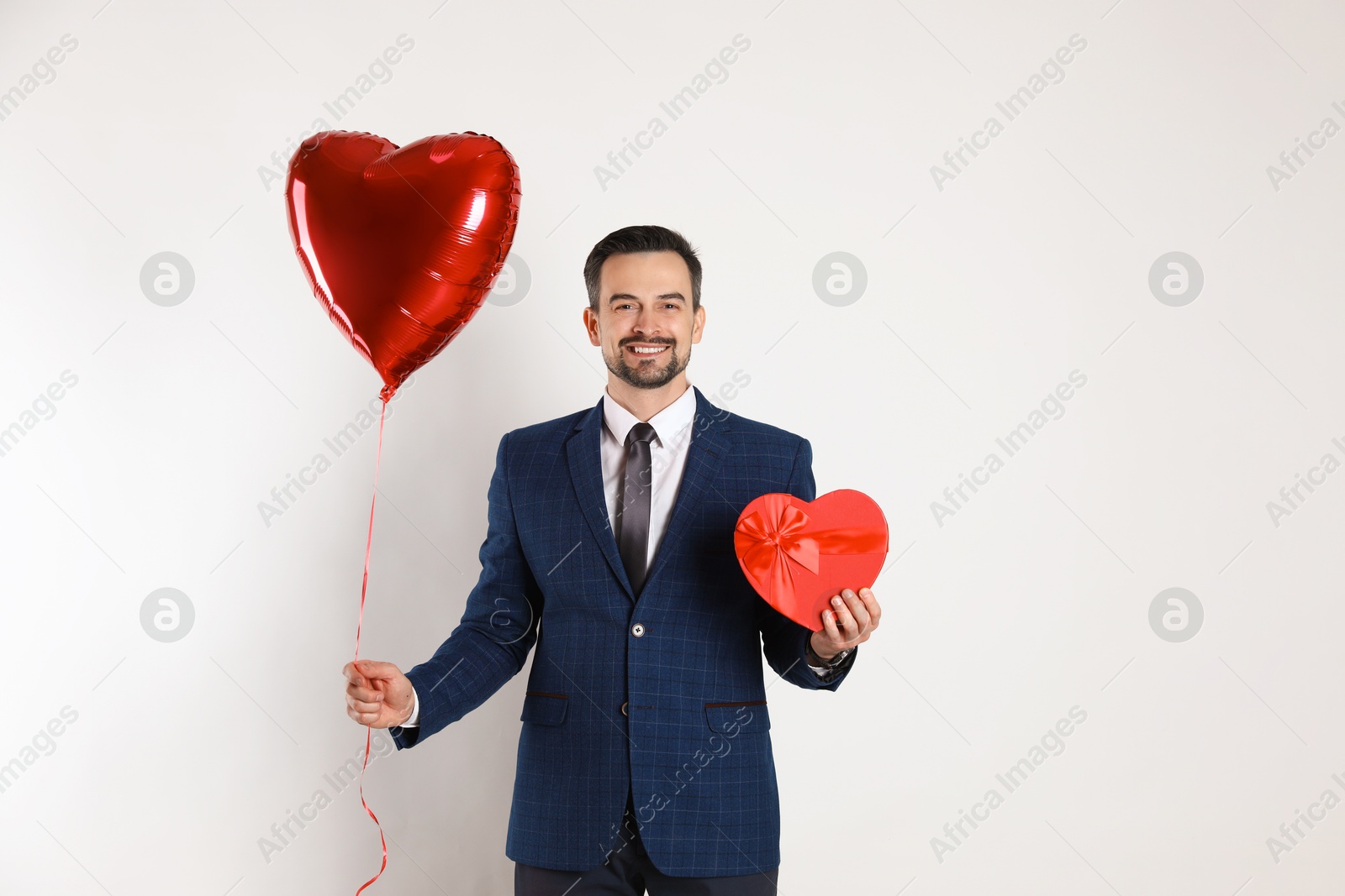 Photo of Happy Valentine's Day. Handsome man with heart shaped balloon and gift box on white background