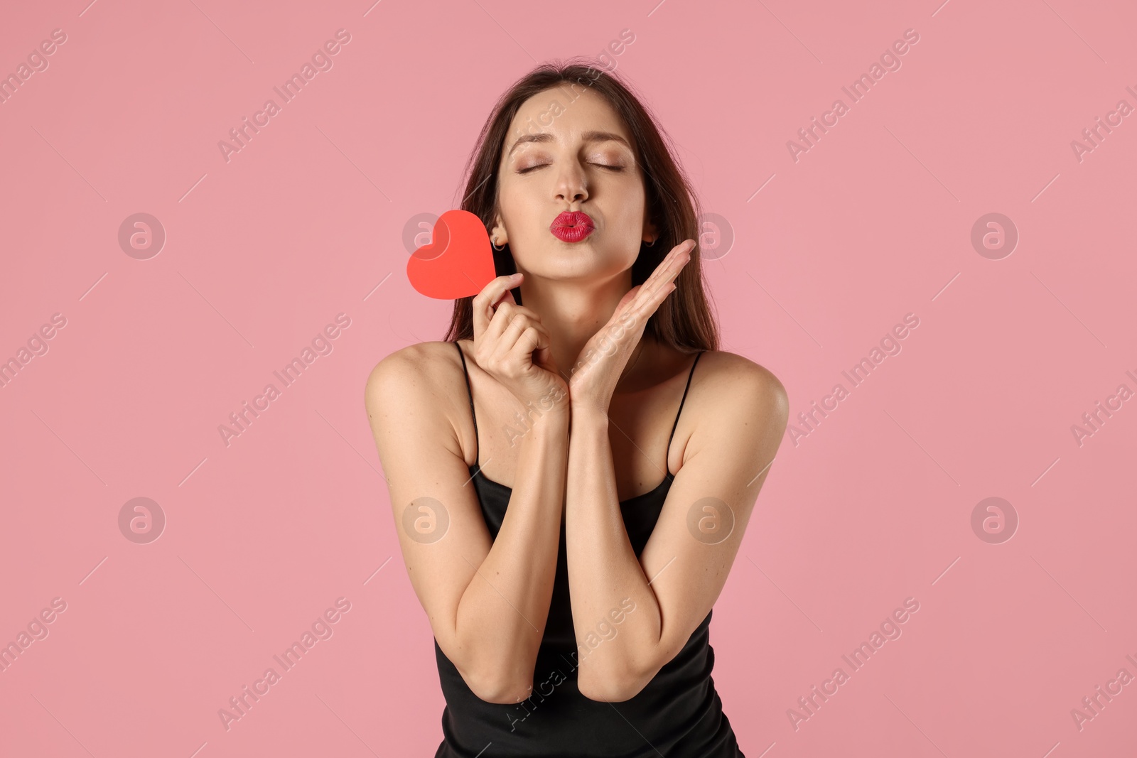 Photo of Happy Valentine's Day. Beautiful woman with paper heart sending air kiss on pink background