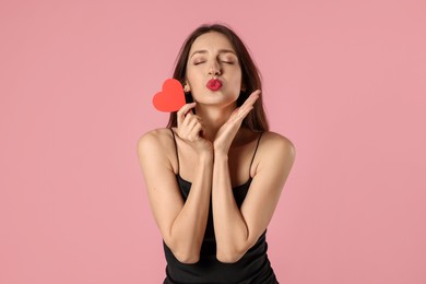 Photo of Happy Valentine's Day. Beautiful woman with paper heart sending air kiss on pink background