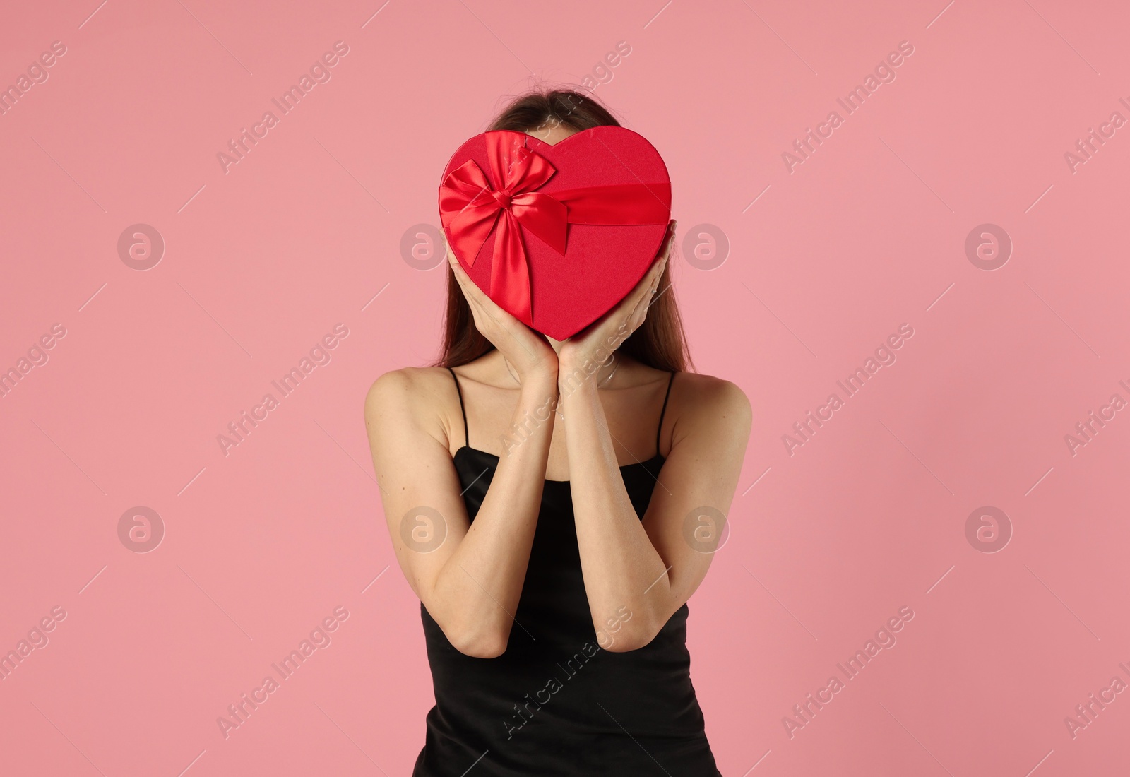 Photo of Happy Valentine's Day. Woman hiding behind heart shaped gift box on pink background