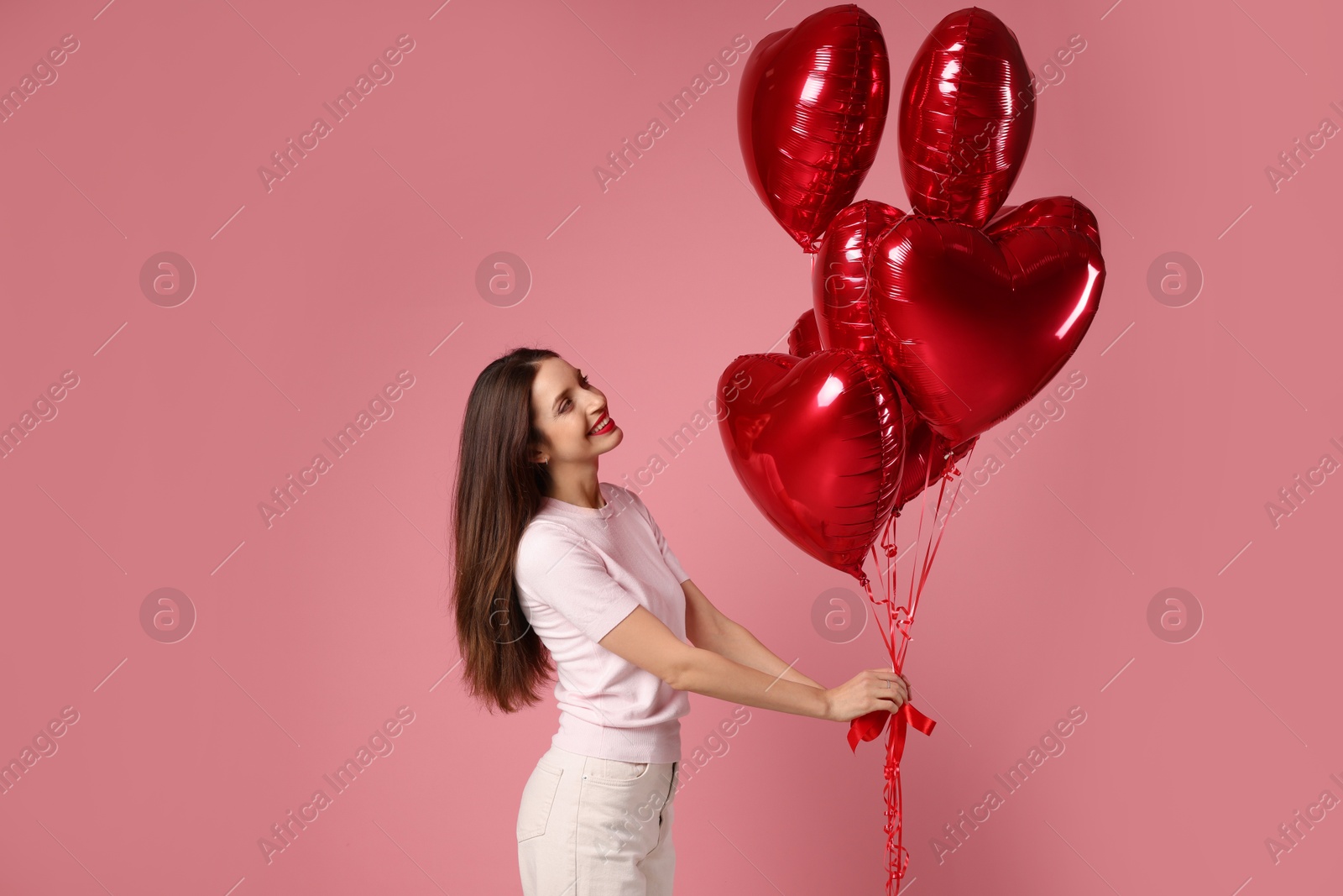 Photo of Happy Valentine's Day. Beautiful woman with heart shaped balloons on pink background