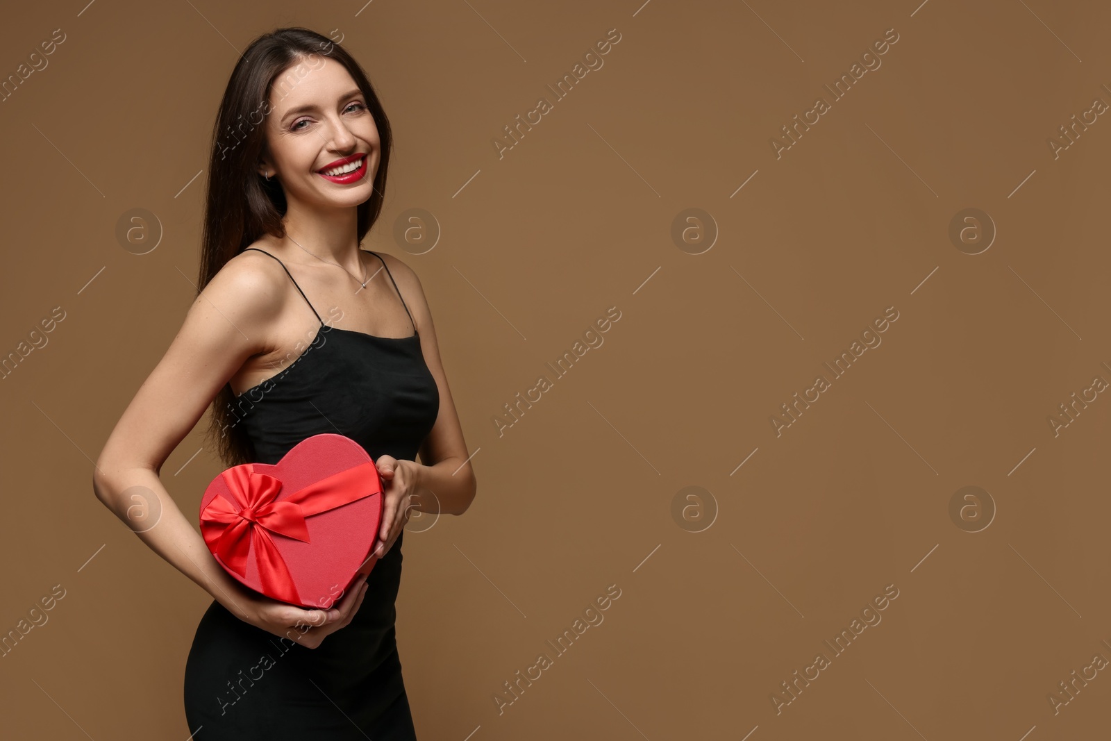 Photo of Happy Valentine's Day. Beautiful woman with heart shaped gift box on brown background. Space for text