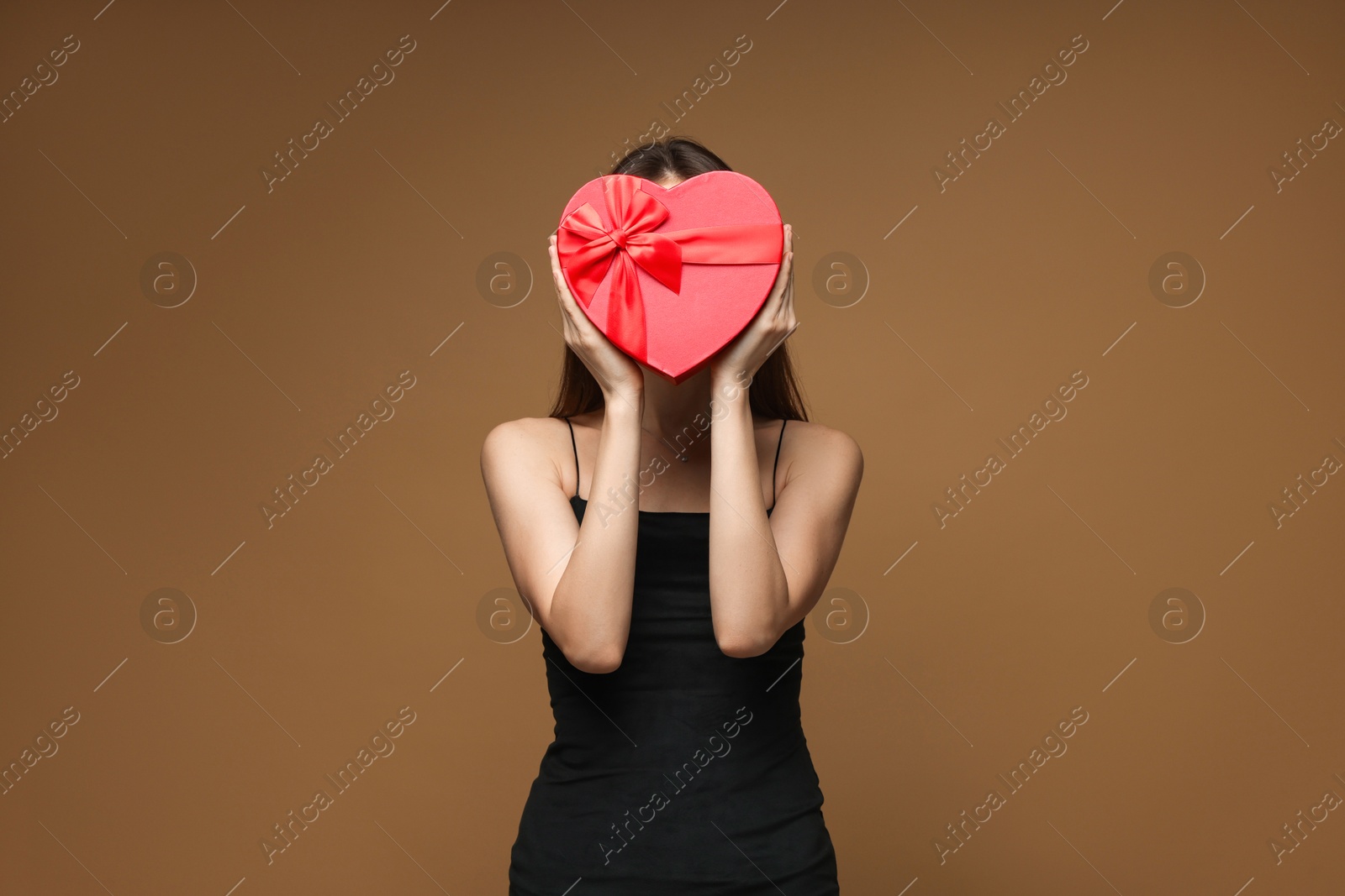 Photo of Happy Valentine's Day. Woman hiding behind heart shaped gift box on brown background