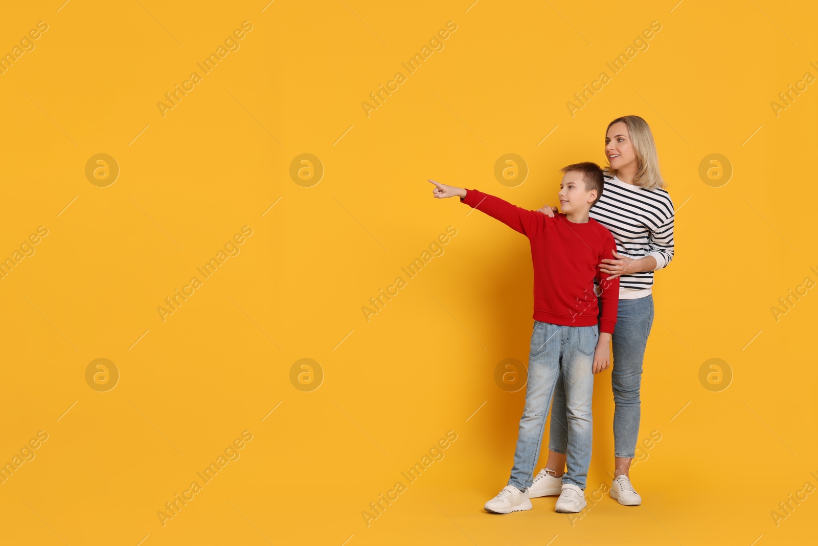 Photo of Son showing his mother something on orange background. Space for text