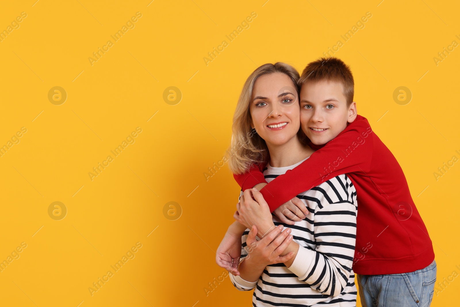 Photo of Mother and son hugging on orange background. Space for text