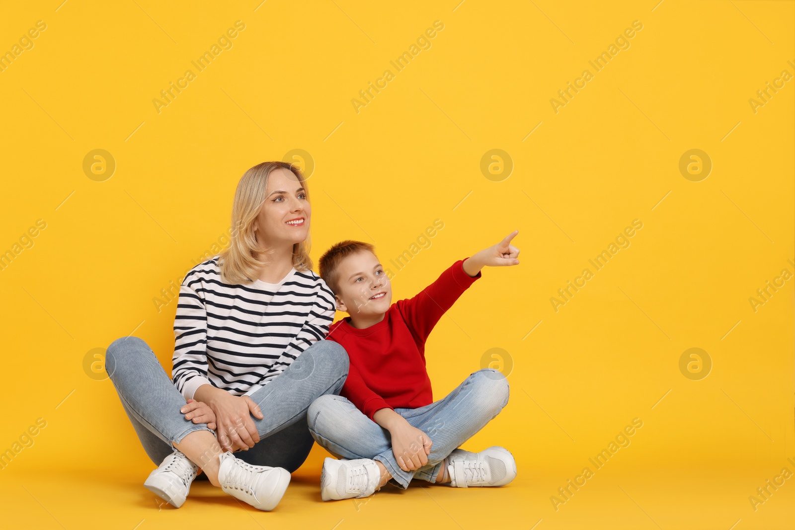 Photo of Son showing his mother something on orange background. Space for text