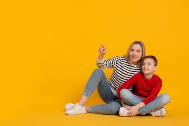 Photo of Son showing his mother something on orange background. Space for text