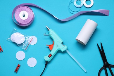 Photo of Hot glue gun and handicraft materials on light blue background, flat lay