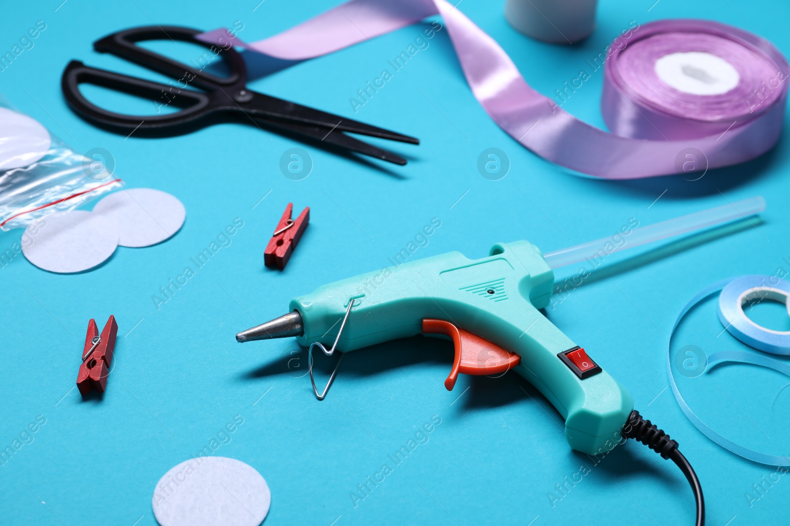 Photo of Hot glue gun and handicraft materials on light blue background