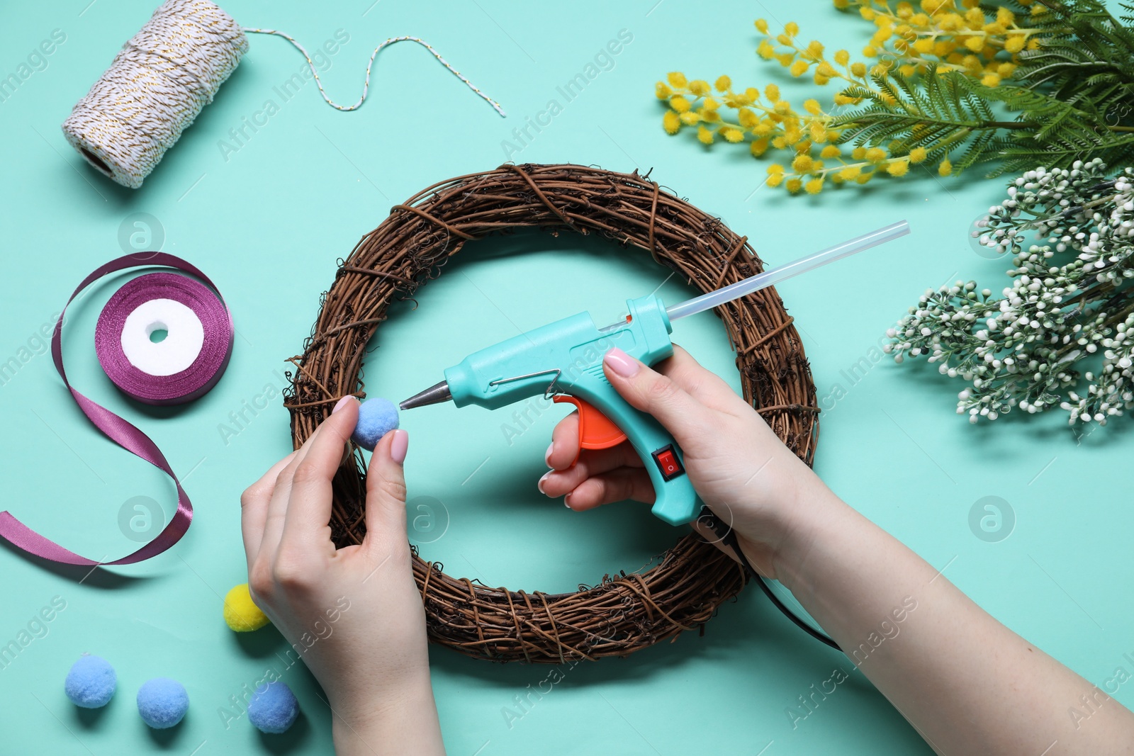 Photo of Woman with hot glue gun making craft on light blue background, top view