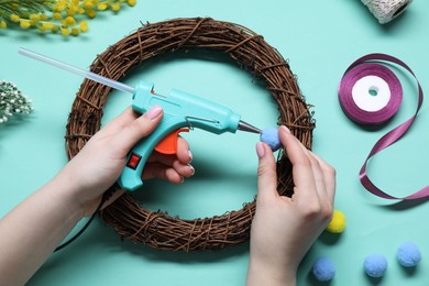 Photo of Woman with hot glue gun making craft on light blue background, top view