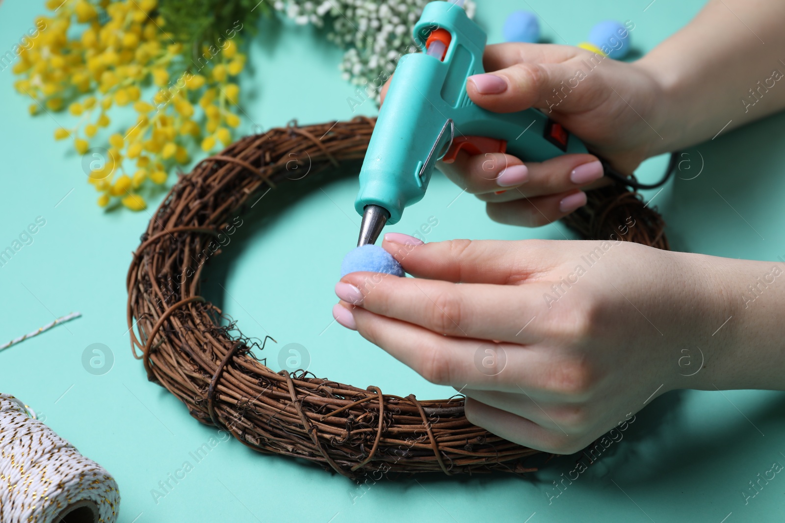 Photo of Woman with hot glue gun making craft on light blue background, closeup