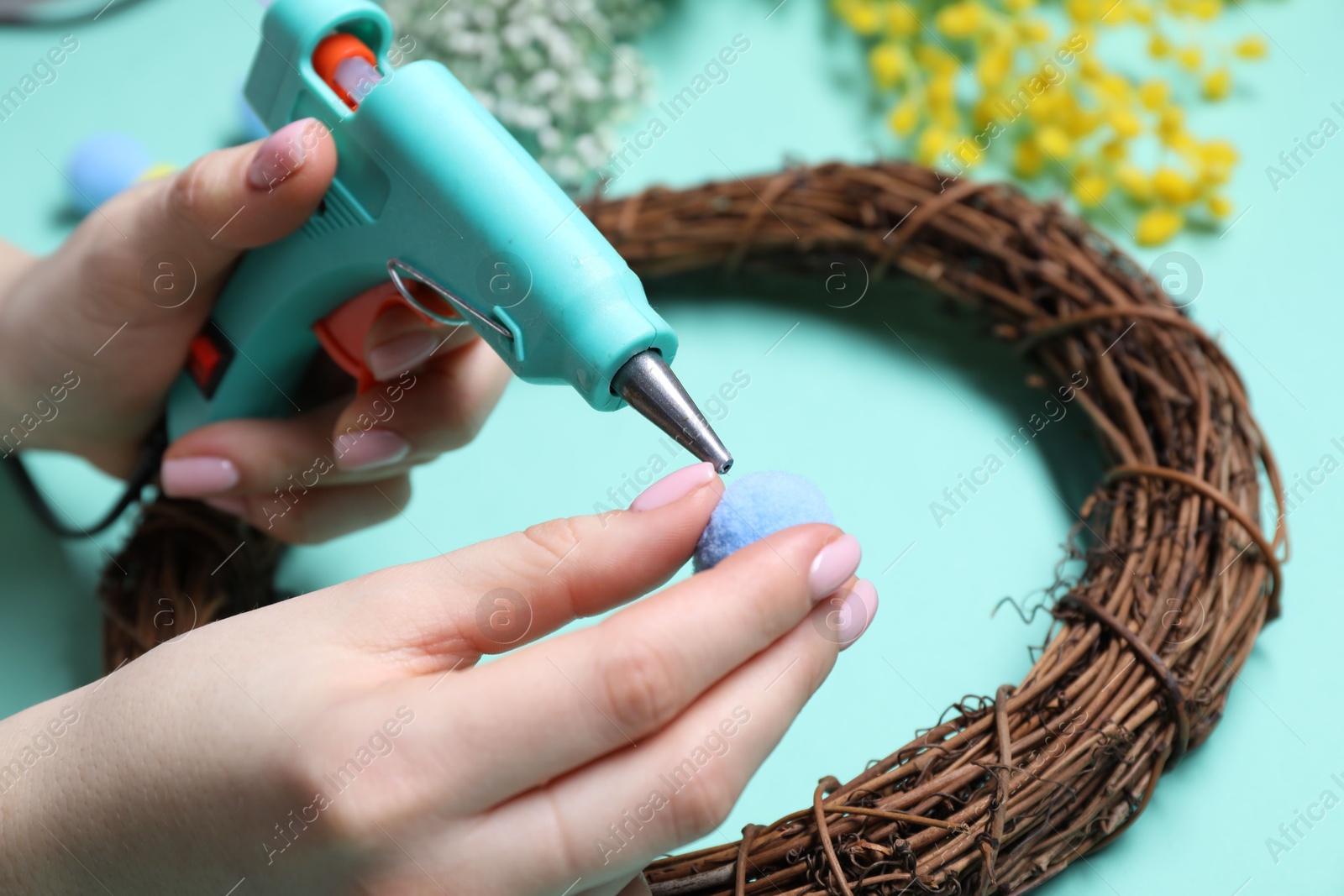 Photo of Woman with hot glue gun making craft on light blue background, closeup