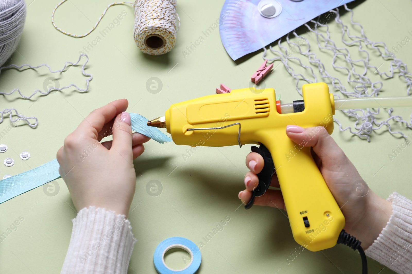 Photo of Woman with hot glue gun making craft on pale olive background, above view