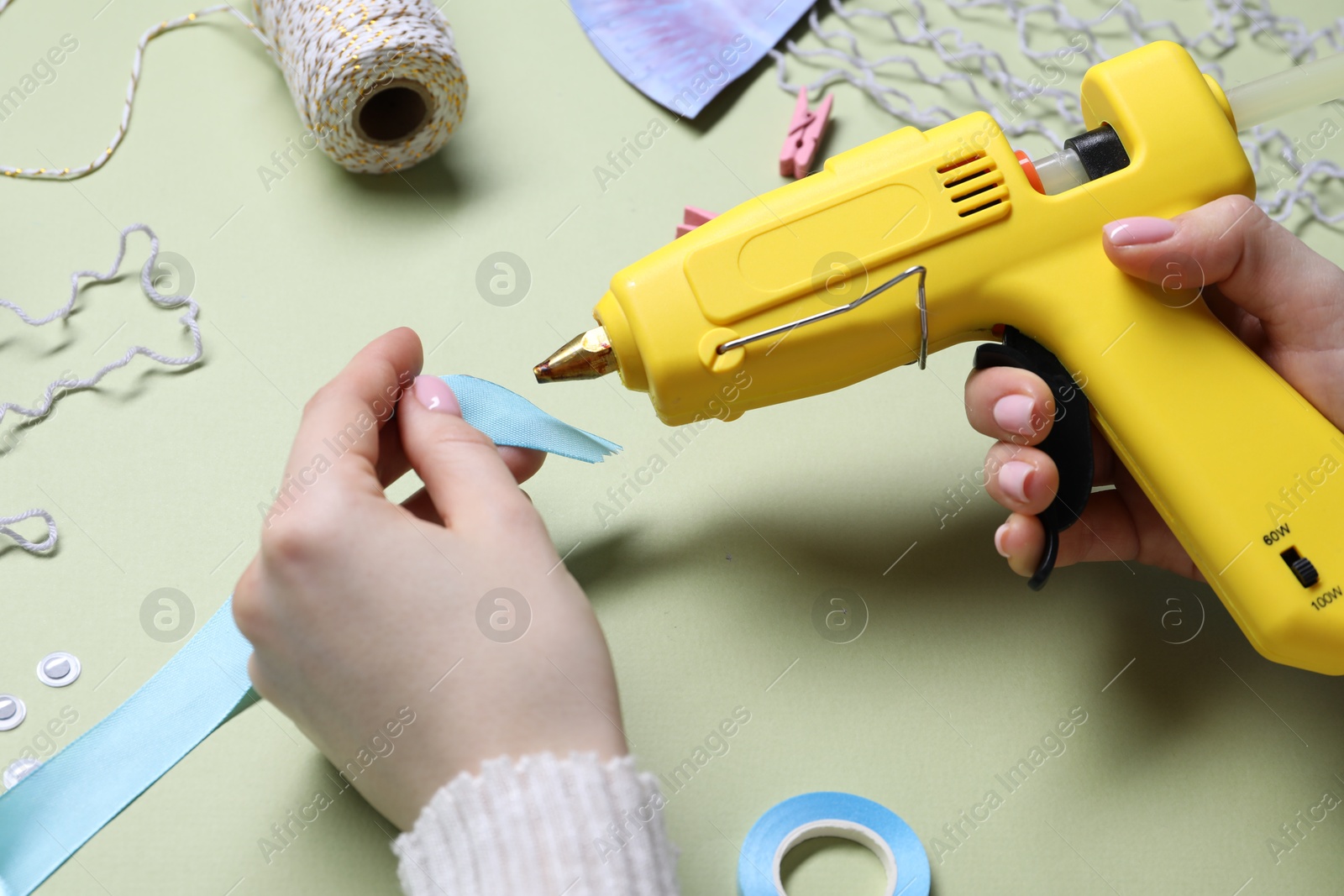 Photo of Woman with hot glue gun making craft on pale olive background, closeup