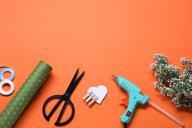 Photo of Hot glue gun and handicraft materials on orange background, flat lay. Space for text