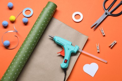 Photo of Hot glue gun and handicraft materials on orange background, flat lay