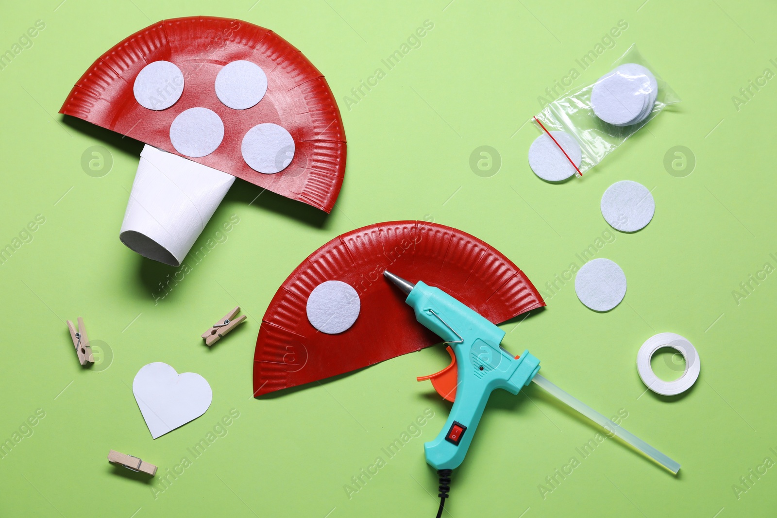 Photo of Hot glue gun and handicraft materials on green background, flat lay