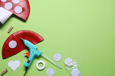 Photo of Hot glue gun and handicraft materials on green background, flat lay. Space for text