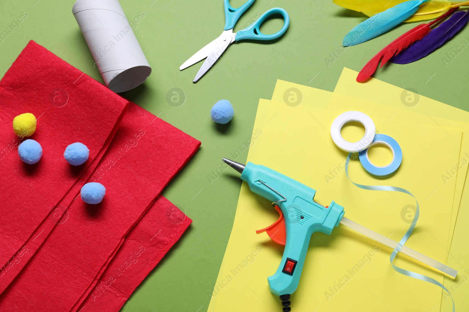 Photo of Hot glue gun and handicraft materials on green background, flat lay