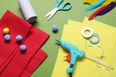 Photo of Hot glue gun and handicraft materials on green background, flat lay