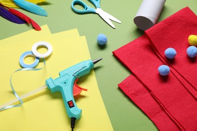 Photo of Hot glue gun and handicraft materials on green background, above view