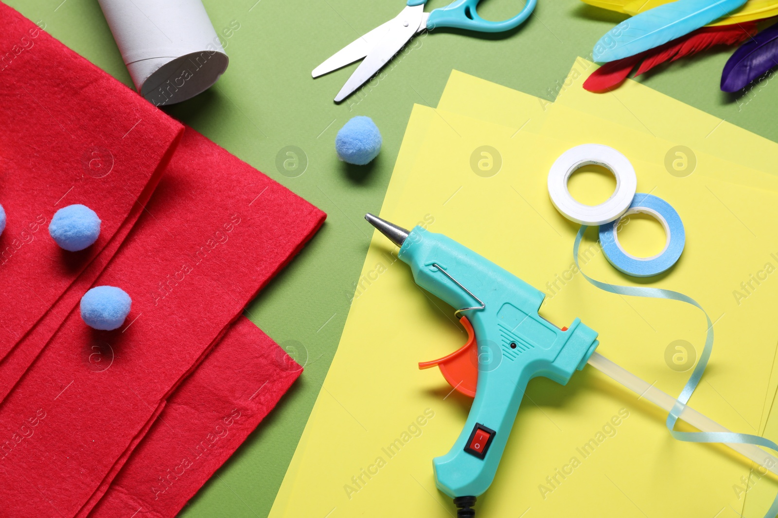 Photo of Hot glue gun and handicraft materials on green background, flat lay