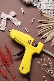 Photo of Hot glue gun and handicraft materials on brown background, flat lay