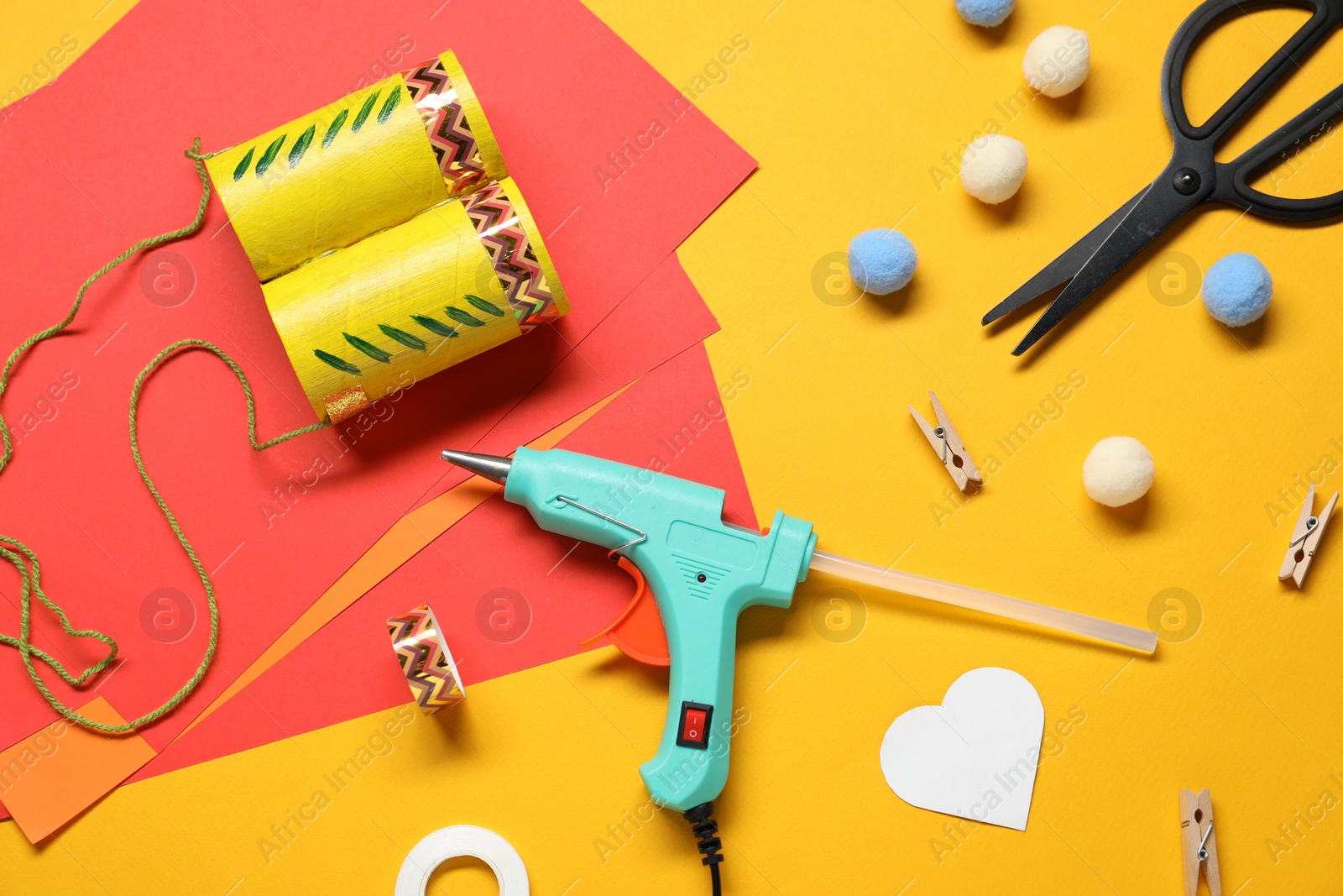 Photo of Hot glue gun and handicraft materials on orange background, flat lay