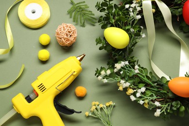 Photo of Hot glue gun and handicraft materials on olive background, flat lay