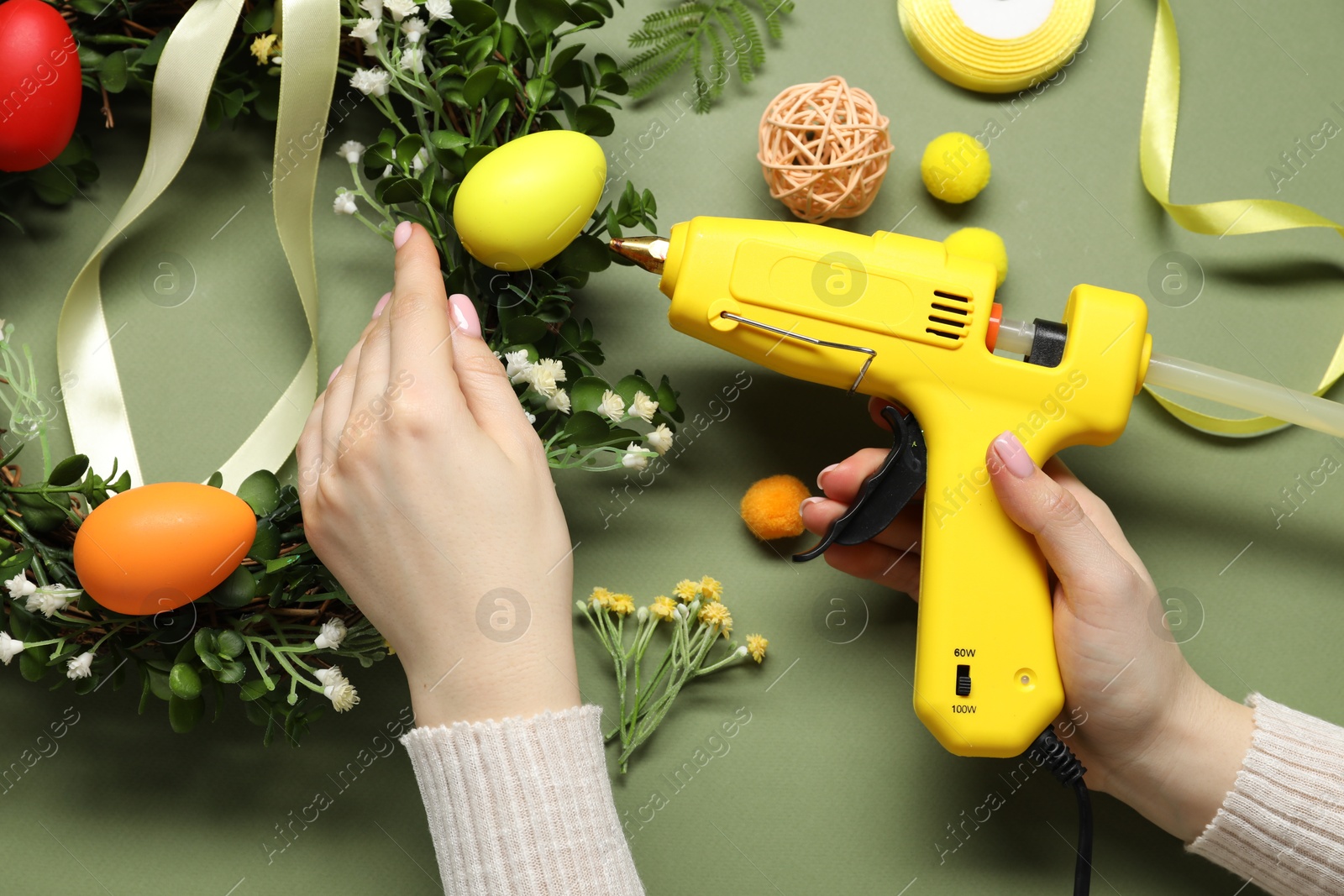 Photo of Woman with hot glue gun making craft on olive background, top view