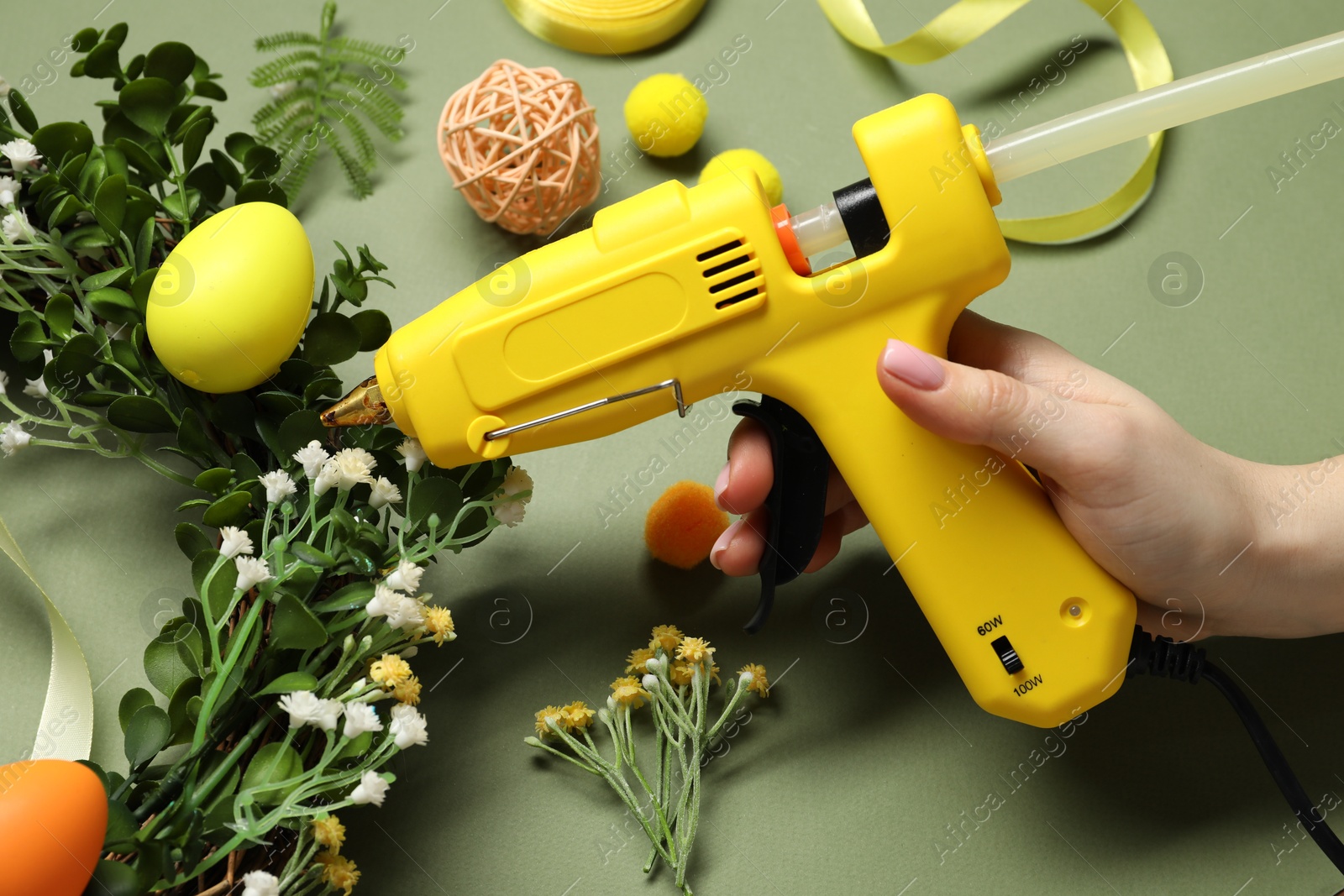 Photo of Woman with hot glue gun making craft on olive background, closeup