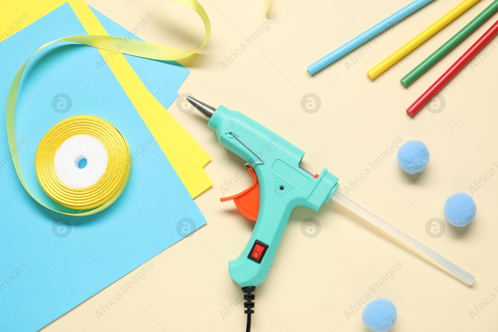 Photo of Hot glue gun and handicraft materials on beige background, flat lay