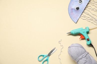 Photo of Hot glue gun and handicraft materials on beige background, flat lay. Space for text