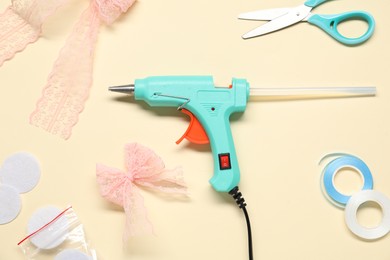 Photo of Hot glue gun and handicraft materials on beige background, flat lay