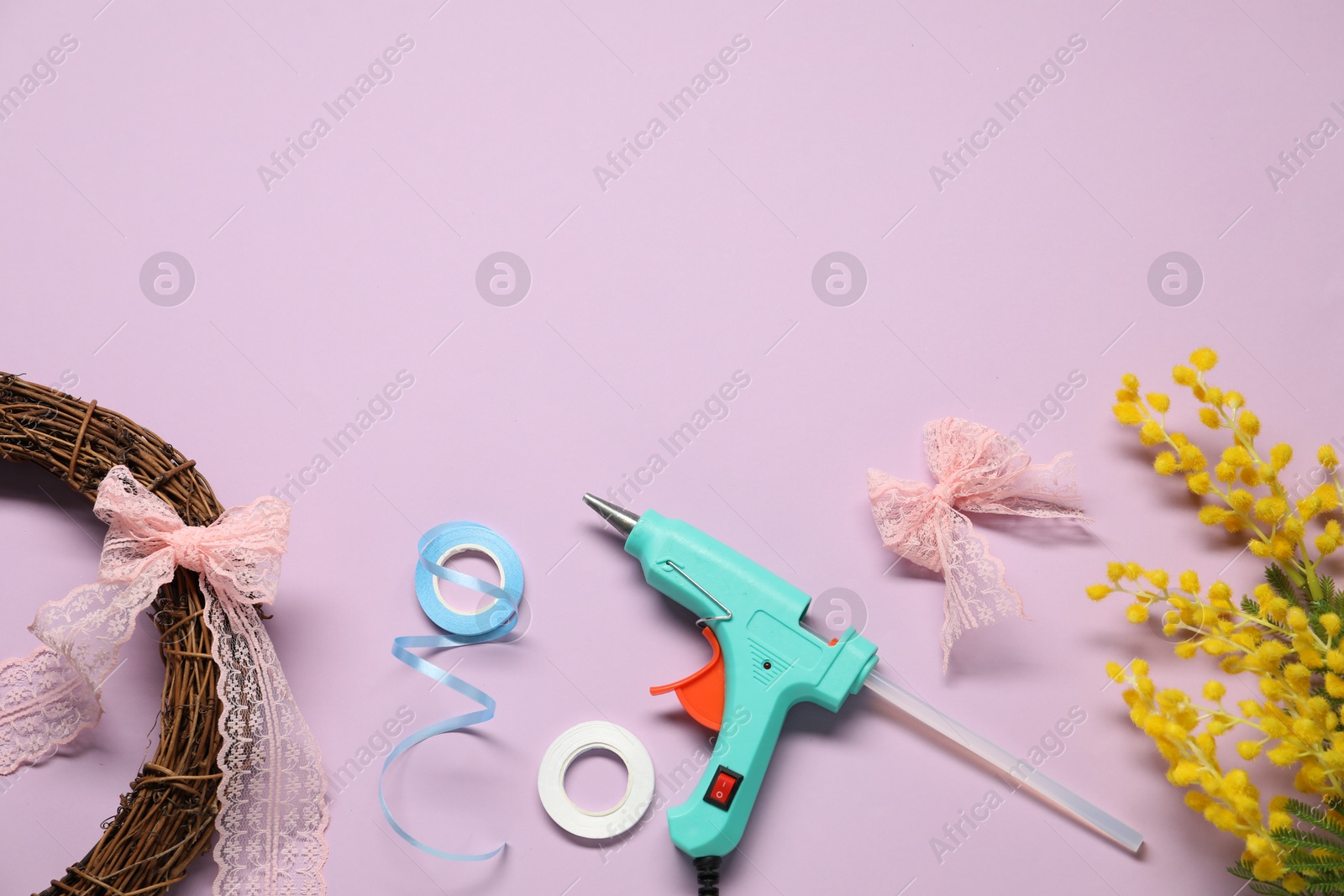 Photo of Hot glue gun and handicraft materials on lilac background, flat lay. Space for text