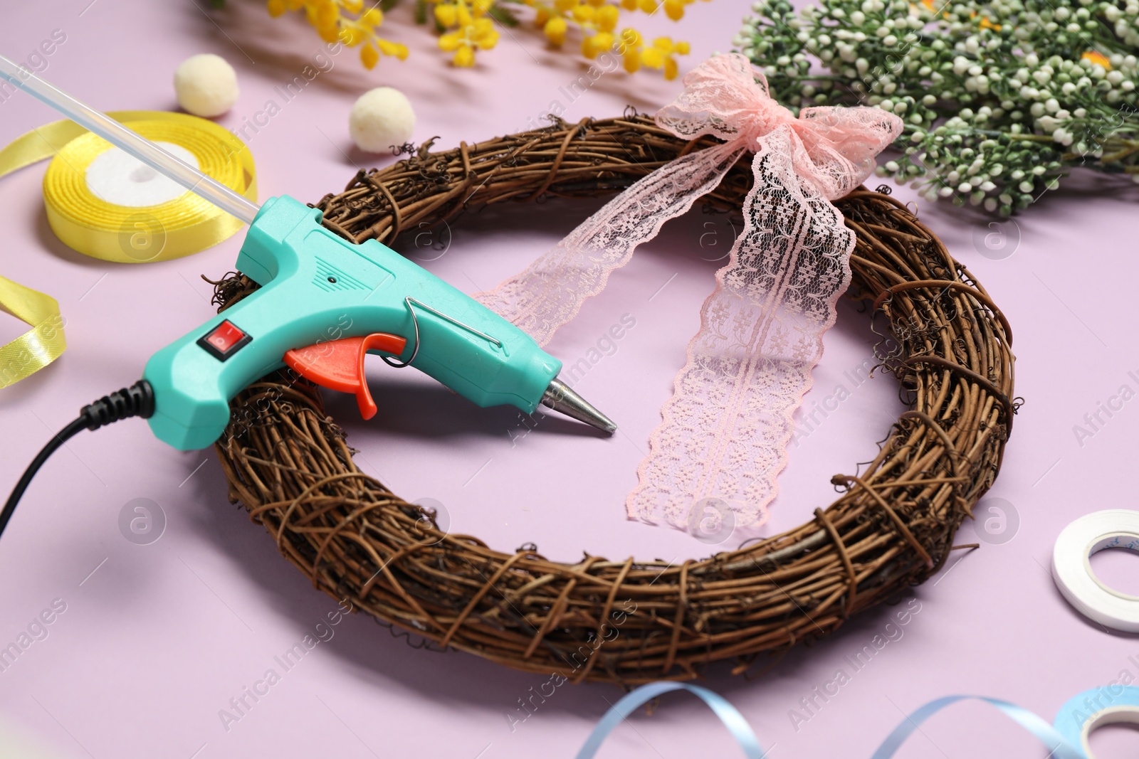 Photo of Hot glue gun and handicraft materials on lilac background, closeup