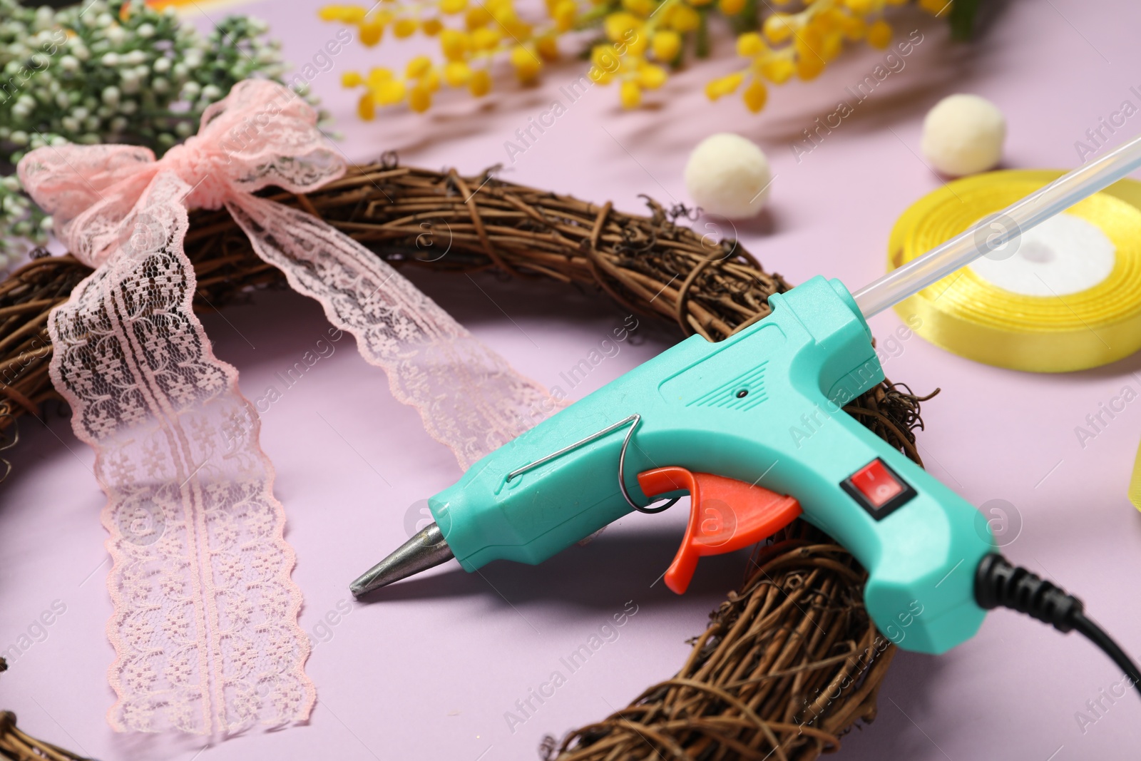 Photo of Hot glue gun and handicraft materials on lilac background, closeup