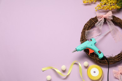 Photo of Hot glue gun and handicraft materials on lilac background, flat lay. Space for text