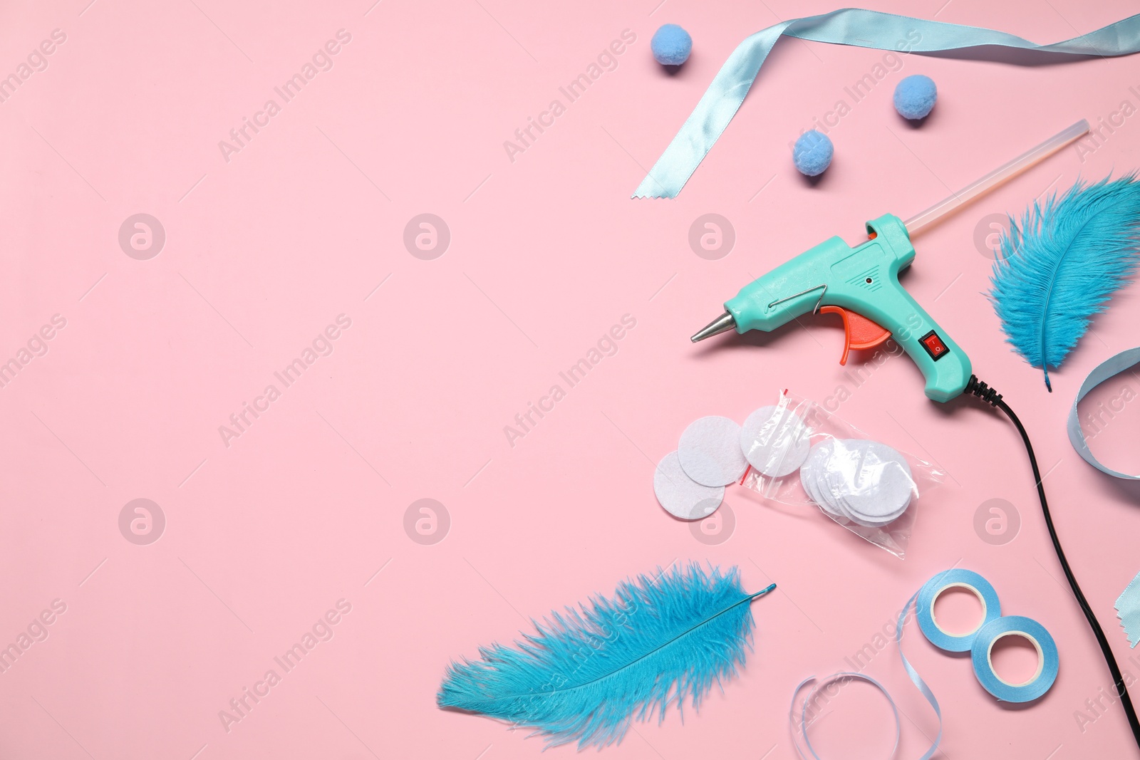 Photo of Hot glue gun and handicraft materials on pink background, flat lay. Space for text