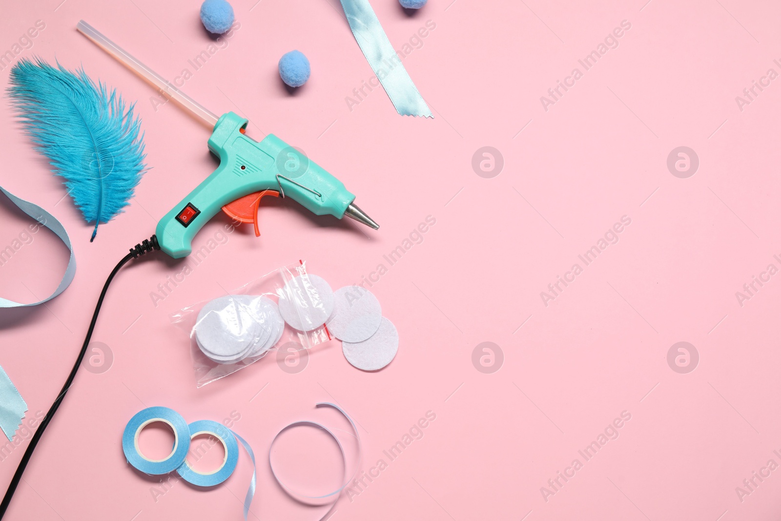 Photo of Hot glue gun and handicraft materials on pink background, flat lay. Space for text